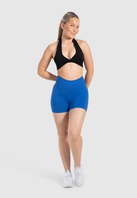 Czarny top na halter z niebieskimi szortami z wysokim stanem, wykonanymi z elastycznego materiału, w połączeniu z białymi trampkami, tworząc sportowy, aktywny wygląd.