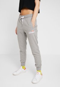 Grå sweatpants med elastisk midjeband och dragsnöre, med sidofickor och en broderad logotyp. Kombinerad med vita sneakers och färgglada strumpor.