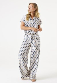 Zweiteiliges Outfit bestehend aus einem kurzärmeligen Oberteil und weiten Hosen, aus leichtem Stoff mit einem blauen und cremefarbenen geometrischen Muster.
