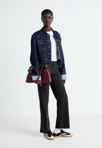 Denimjacka med blå tvätt, vit t-shirt, grå randiga byxor, svarta och krämfärgade sneakers, och en vinröd axelväska.