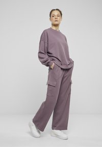 Lila matchande sweatshirt och vida byxor i mjuk tyg, med framfickor och rundad nacke, tillsammans med vita sneakers.
