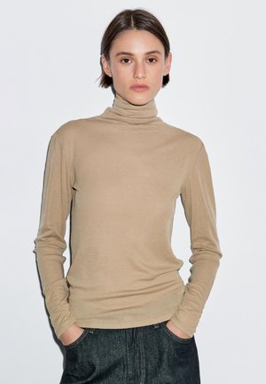 Beżowy sweter z golfem wykonany z miękkiego materiału, z długimi rękawami, cechujący się dopasowanym krojem, gładką teksturą i prostym, bezszwowym dekoltem.