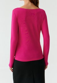 Väriltään kirkkaan pinkki, pehmeästä kankaasta valmistettu pitkähihainen pääntie. Varustettu leveällä kaula-aukolla ja sileillä saumoilla, yhdistetty mustaan hameeseen.