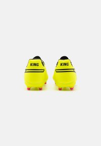 Žlté futbalové kopačky s čiernymi akcentmi, zobrazujúce logo "KING" na päte a ružovými kolíkmi na spodnej strane pre lepšiu trakciu.