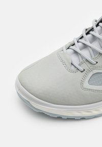Light gray athletic shoe with textured synthetic upper, mesh panels, and gray laces, featuring a rubber sole with a slight translucent edge.