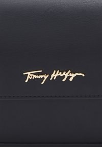 Surface en cuir noir avec un logo en cursive dorée de Tommy Hilfiger centré au-dessus d'une couture.