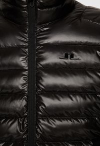 Svart uppblåsbar jacka med en slät, glänsande yta, horisontella quiltade paneler och en framfickare. Kort krage med logotypdetalj.