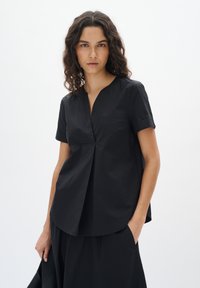 Top nero a maniche corte con scollatura a V e dettagli arricciati nella parte anteriore. Tessuto leggero con una texture liscia, silhouette aderente.