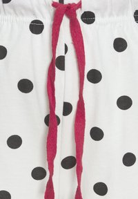 Vita tygshorts med stora svarta prickar, med en röd snörning i midjan. Slät textur med elastisk midjeband.