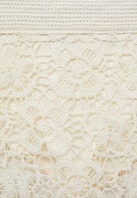 Țesătură albă din dantelă, cu modele florale cu detalii și texturi intricate, așezată deasupra unui fundal solid crem.