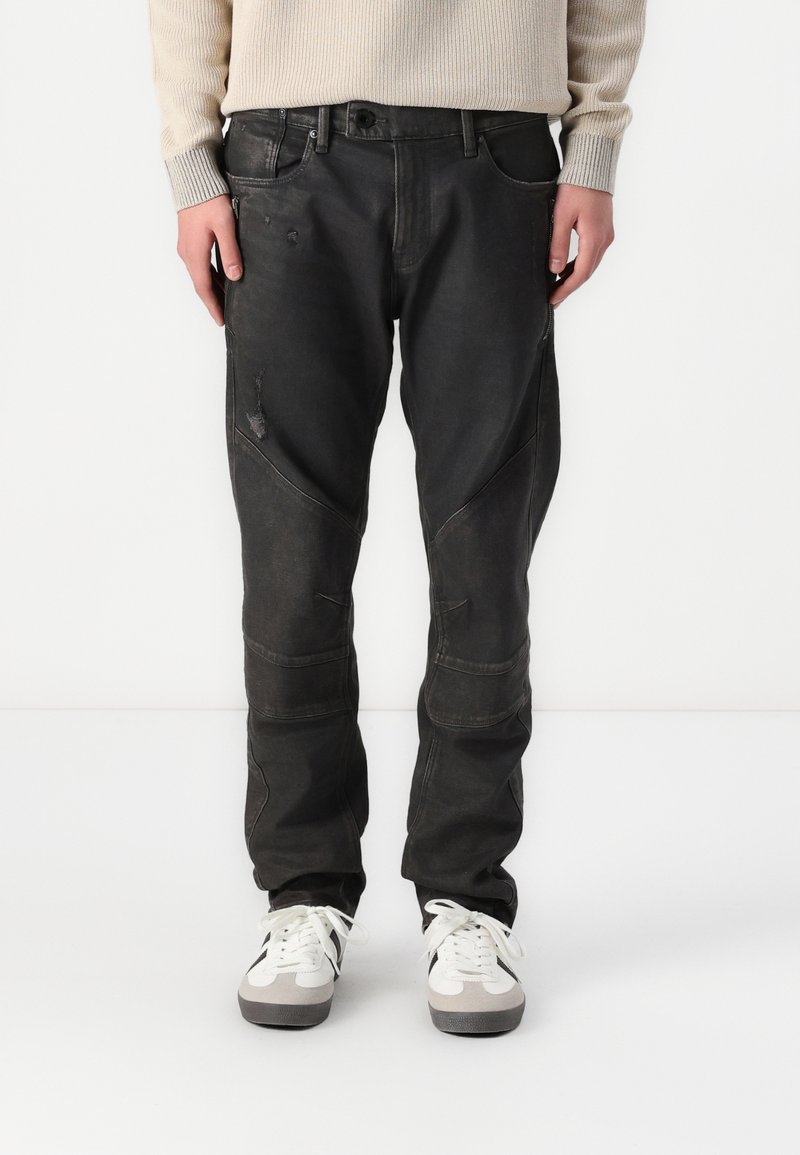 Pantalones de mezclilla negra con un corte holgado, que presentan un ligero desgastado, costuras curvadas y múltiples bolsillos. Combinados con zapatillas blancas.