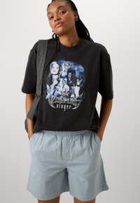 Svart grafisk t-shirt med blå och vit "Buffy the Vampire Slayer" design. Ljusblåa strukturerade shorts med elastisk midja och fickor.