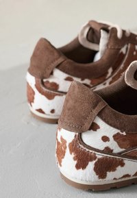 Ruske mokasiner u nubuk koži sa bijelim i smeškim točkicama od kravljeg krzna. Zaobljenog oblika sa kontrastnim teksturama i šavovima na peti.