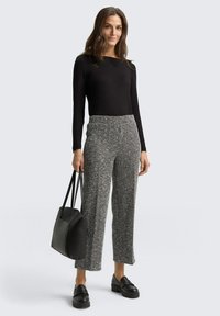 Zwarte lange mouwen top gecombineerd met grijze houndstooth-gepatroonte wijde broek. Zwarte totebag en chunky zwarte loafers maken de outfit compleet.