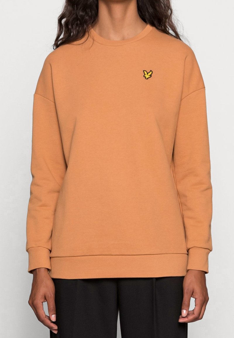 Sudadera naranja con cuello redondo, diseño holgado, puños acanalados y un pequeño logo de pájaro amarillo en el pecho. Acabado textil suave.