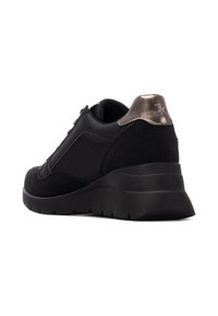 Zapatilla deportiva negra con parte superior de ante y sintético, punta redondeada, acento metálico en el talón y suela de goma gruesa.