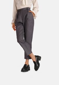 Pantaloni grigi su misura con vita alta e tasche laterali, abbinati a mocassini in pelle nera con suola spessa.