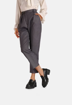 Pantaloni grigi su misura con vita alta e tasche laterali, abbinati a mocassini in pelle nera con suola spessa.