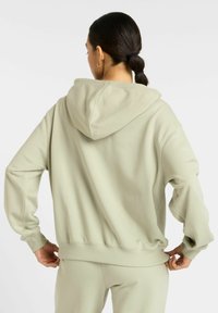 Hoodie vert clair avec une grande capuche, coupe décontractée et poignets côtelés. Matière en coton doux avec une texture lisse et des coutures minimales.