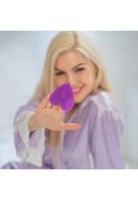 Fioletowy aplikator wykonany z silikonu w kształcie serca, trzymany w dłoni, z teksturowaną powierzchnią, wyraźnie widoczny na miękkim tle.