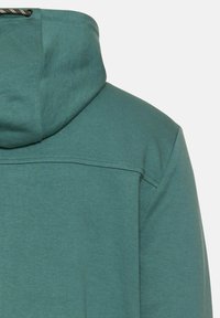 Sweatshirt vert avec capuche, texture lisse, coutures renforcées et design simple, avec un détail de cordon de serrage au niveau du cou.