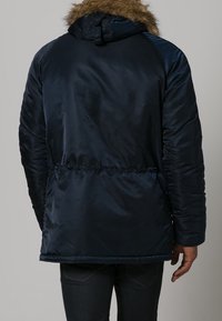 Navy blue puffer jacket with a fur-lined hood, featuring a smooth, shiny texture and elastic cuffs. Visible stitching at the waist.