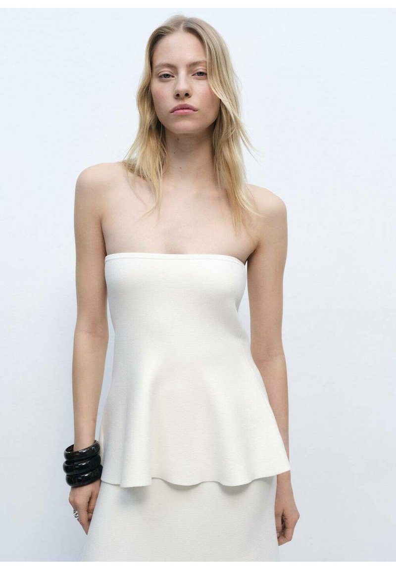 Strapless crèmekleurig top van textuurstof met een uitlopende zoom, met een soepele silhouet, gedragen met zwarte ronde armbanden om de pols.