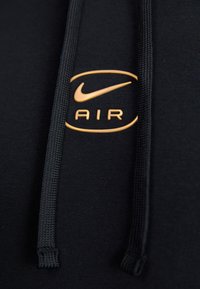 Black hoodie with a textured fabric. Features a gold Nike logo with "AIR" in a circular design, and dark drawstrings.