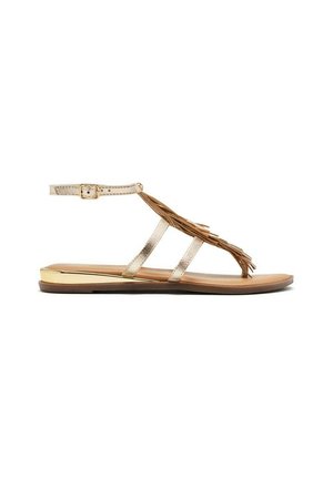 Sandalias planas metálicas doradas con suela marrón, que presentan tres tiras y un detalle decorativo de flecos. Correa ajustable en el tobillo para un mejor ajuste.