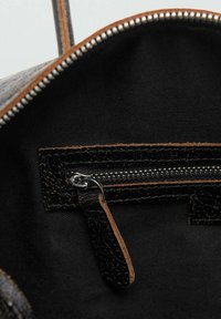Interior de un bolso de tela negra con un pequeño bolsillo con cremallera, que cuenta con un borde de cuero negro texturizado y un tirador de cremallera plateado.