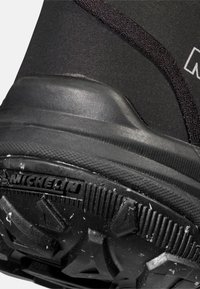 Svart vinterkänga i närbild, med en texturerad gummisula med djupa mönster, förstärkt häl och överdel i elastisk tyg. Michelin-logotyp synlig.