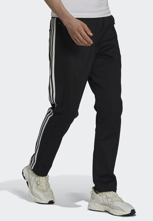 Pantaloni sportivi neri con strisce laterali bianche, vita elasticizzata e tasche con zip, realizzati in un materiale leggero e liscio.