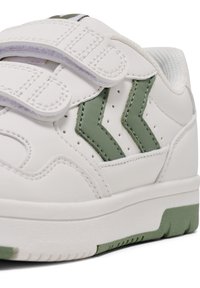 Weiße Sneaker mit grünen Akzenten, glattes synthetisches Obermaterial, perforierte Seite zur Belüftung und zwei verstellbare Klettverschlüsse. Texturierte Sohle.