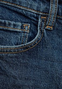 Tissu en denim bleu avec des coutures visibles en fil doré. Présente une ouverture de poche et une ceinture avec une texture lisse.