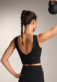 Un sutien sport negru cu un design adânc în V la spate. Prezintă o siluetă ajustată și o textură netedă, asortat cu colanți negri cu talie înaltă.