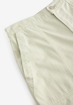 Jasnobeżowe spodnie z wysokim stanem z przednimi kieszeniami i metalowym guzikiem, pokazane z bliska na białym tle.