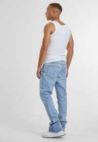 Lys blå denim jeans med avslappet passform, med femlommersdesign og subtile sømmer. Brukt med en hvit tanktop og sneakers.