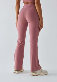 Różowe legginsy dzwony wykonane z elastycznego materiału, z wysokim stanem i gładką fakturą, zestawione z jasnymi sneakersami.