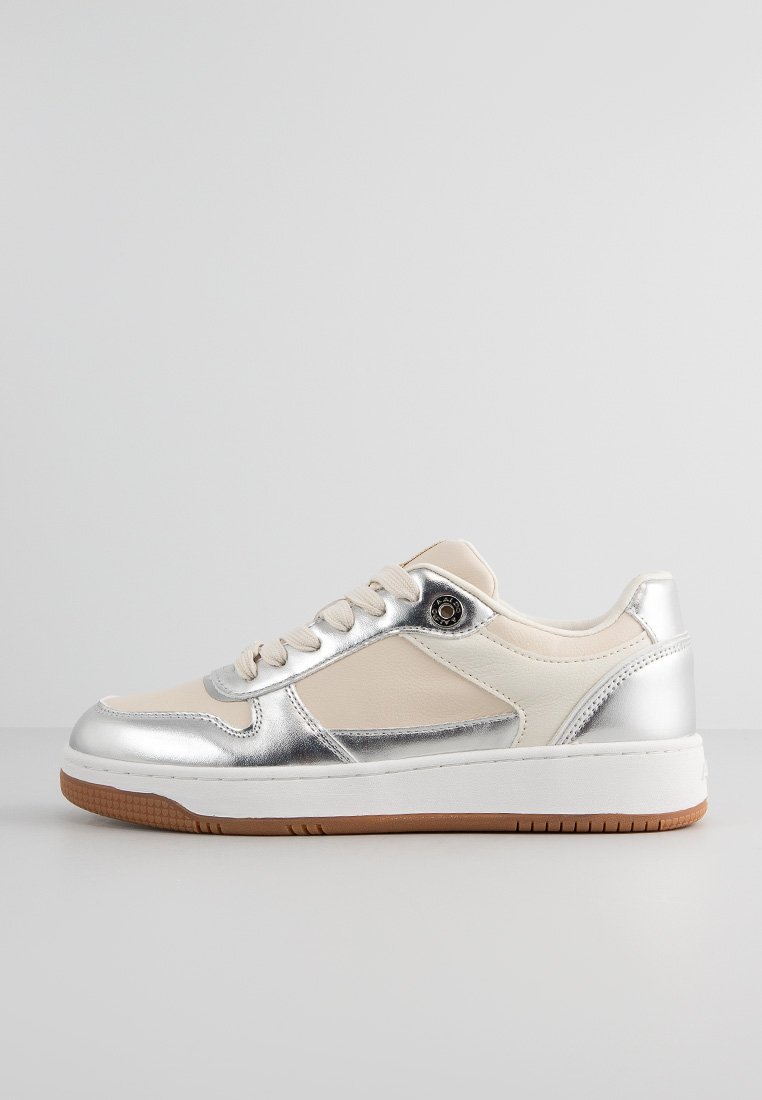 Sneaker basse en beige et argent métallique, avec des lacets blancs, une semelle épaisse et une semelle extérieure en caoutchouc marron, présentée de côté sur un fond neutre.