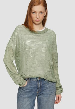 Pull en maille vert clair avec une coupe ample et carrée, présentant un motif texturé et des manches longues, associé à un jean bleu.