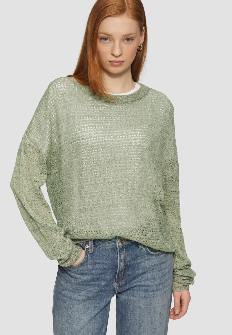 Hellgrüner, gestrickter Pullover in lockerer, kastiger Form mit strukturiertem Muster und langen Ärmeln, kombiniert mit blauen Jeans.