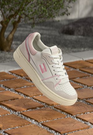 White and light pink Tommy Jeans sneaker with laces, perforated toe, and suede accents, hovering above wooden tile flooring outdoors.