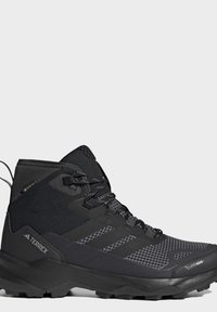 Black high-top hiking shoe with textured sole, branded Terrex and Gore-Tex labels, designed for outdoor and cold weather use.