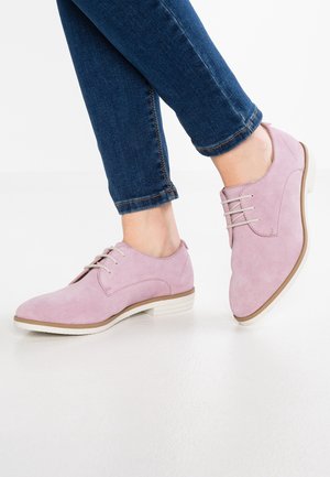 Chaussures à lacets en daim rose clair avec un bout arrondi, une semelle blanche et des détails de couture subtils. Associées à un jean en denim foncé.