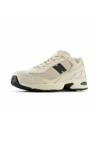 Beige atletisk sko med överdel i mesh och mocka, svarta detaljer, rund tå och dämpad sula. Har snörning och strukturerad gummisula.