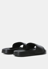 Black slide sandals with a textured upper, open toe design, and a thick rubber sole. Features a logo on the strap and soft interior lining.