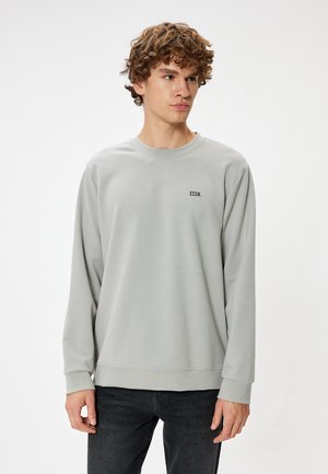 Lys grå sweatshirt med lange ærmer, rund hals og ribbede manchetter. Har et lille sort "ESSN." logo på forsiden. Blød tekstur.