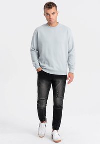 Sudadera azul claro con cuello redondo y puños acanalados, combinada con jeans negros desgastados y zapatillas blancas con suelas marrones.