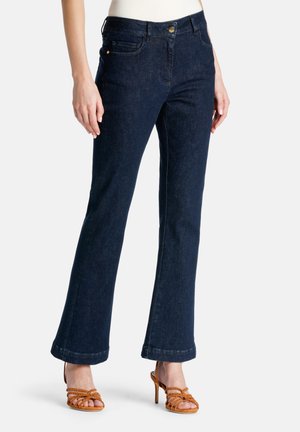 Jeans acampanados de color azul oscuro hechos de denim, con bolsillos frontales, cierre de botón y un ajuste entallado, combinados con tacones marrones con tiras.