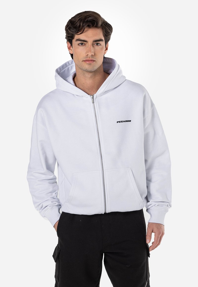 Hvid zip-up hættejakke med en frontlomme og logo-tekst. Har en hætte med snore og ribbede manchetter. Fremstillet af blødt bomuldsstof.